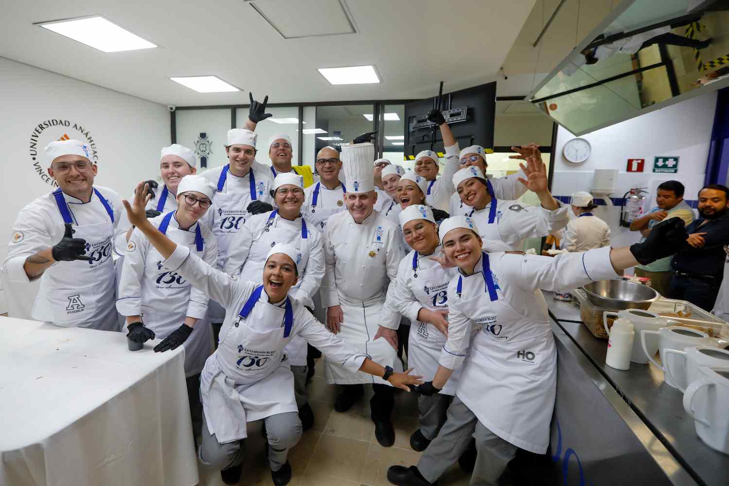 Estudiantes de gastronomía y chefs posando sonrientes en una cocina profesional.